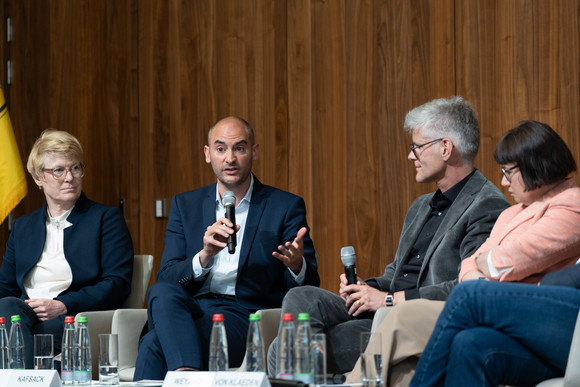 Der Finanzminister beantwortet auf dem Podium eine Frage des Moderators, die weiteren Panelisten hören zu.