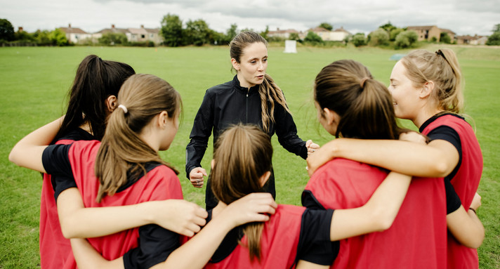 Eine Trainerin bespricht sich auf dem Feld mit ihrer Mannschaft / Foto: stock.adobe.com / rawpixel