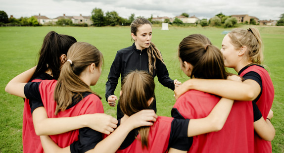 Eine Trainerin bespricht sich auf dem Feld mit ihrer Mannschaft / Foto: stock.adobe.com / rawpixel