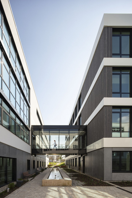 Hochbau Neues Büro- und Laborgebäude für die LUBW Innenhof des neuen Büro- und Laborgebäudes der Landesanstalt für Umwelt Baden-Württemberg (LUBW) in Karlsruhe mit überdachtem Verbindungssteg zwischen zwei Gebäudeteilen und länglichem Wasserbecken im Zentrum. Eine Person überquert den Steg.