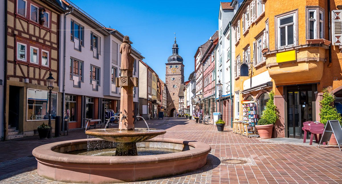 Historische Altstadt mit Brunnen, Fachwerkhäusern und Stadtturm an einem sonnigen Tag.