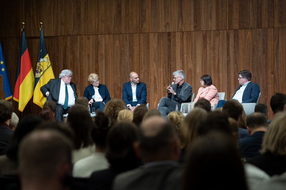 Die Panelisten diskutieren auf dem Podium, im Vordergrund ist das Publikum zu sehen.