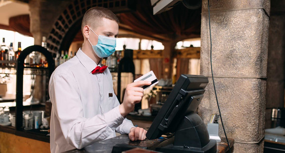 Ein Mann mit Mundschutz steht an einer Kasse in einem Restaurant.