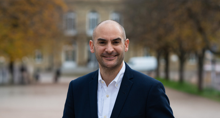 Finanzminister Danyal Bayaz am Schlossplatz in Stuttgart, im Hintergrund das Neue Schloss sowie herbstliche Bäume.