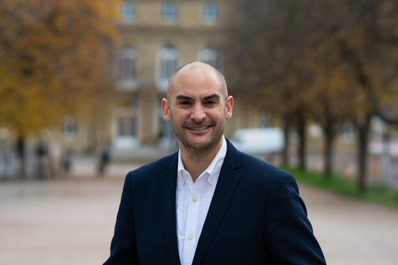 Finanzminister Danyal Bayaz am Schlossplatz in Stuttgart, im Hintergrund das Neue Schloss sowie herbstliche Bäume.