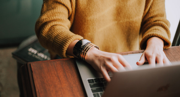 Frau mit gelbem Pullover sitzt am Laptop