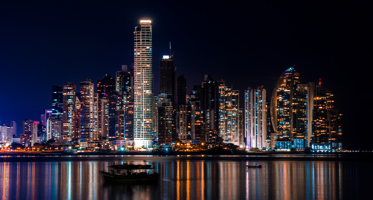 Beleuchtete Skyline einer modernen Großstadt bei Nacht mit Hochhäusern und Spiegelungen im Wasser.