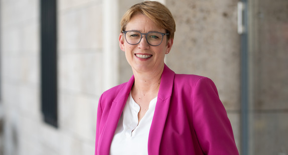 Andrea Lindlohr steht lächelnd vor einer modernen Gebäudefassade.
