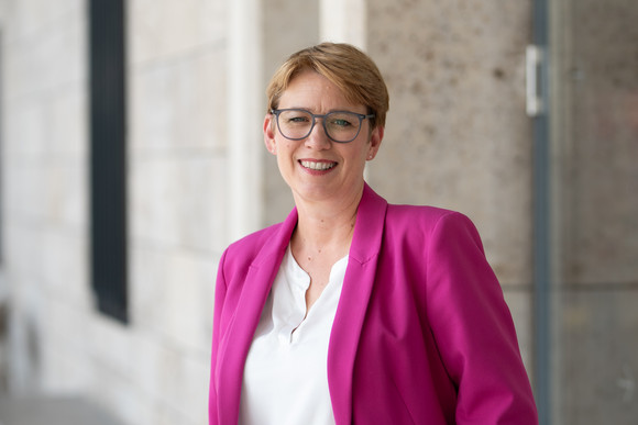 Andrea Lindlohr steht lächelnd vor einer modernen Gebäudefassade.