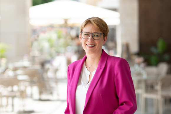 Andrea Lindlohr lächelt vor einer Außengastronomie am Schlossplatz in Stuttgart.