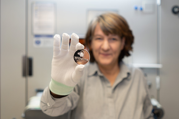 Staatssekretärin Gisela Splett hält die Rückseite der frisch geprägten Medaille (das Logo der Wilhelma) in die Kamera.