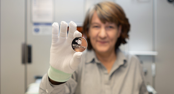 Staatssekretärin Gisela Splett hält die Rückseite der frisch geprägten Medaille (das Logo der Wilhelma) in die Kamera.