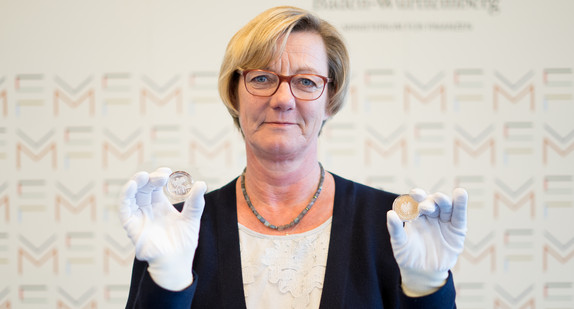 Finanzministerin Edith Sitzmann hält zwei 20-Euro-Silbermünzen „Frau Holle“ in die Kamera. Zu sehen ist einmal die Vorderseite der Münze und einmal die Rückseite.