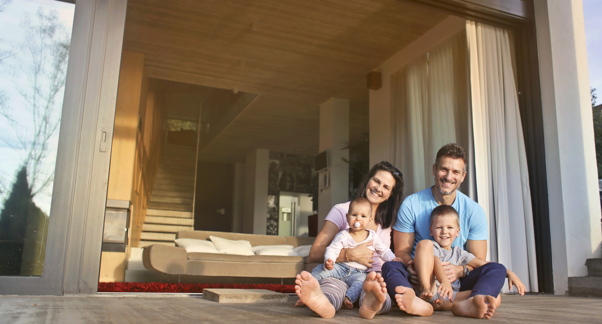 Famile mit zwei Kindern sitzt auf dem Boden vor einem Haus