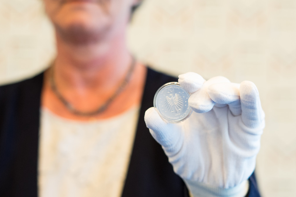 Finanzministerin Edith Sitzmann hält die 20-Euro-Silbermünze „Frau Holle“ in die Kamera