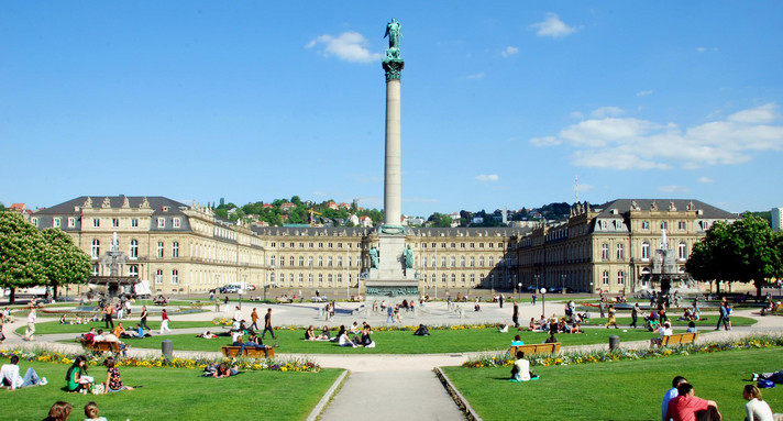 Schlossplatz Stuttgart mit Jubiläumssäule, Grünflächen und Menschen.