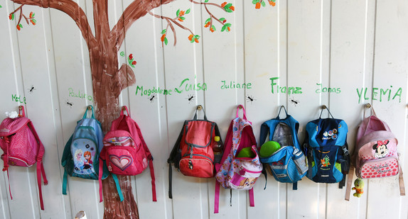 Rucksäcke von Kindern einer Kita hängen an einer Garderobe.