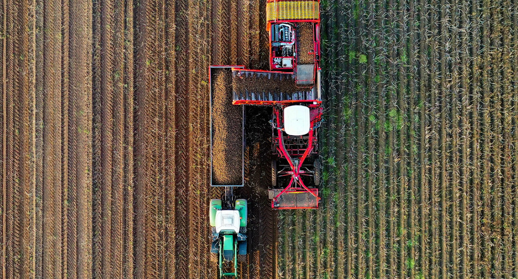 Ein Mähdrescher und ein Traktor auf einem Feld, aufgenommen aus der Vogelperspektive.