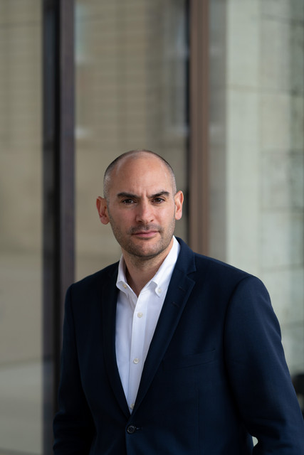 orträt von Finanzminister Danyal Bayaz vor dem Kunstgebäude am Schlossplatz in Stuttgart, mit Glasfassade und Steinstruktur im Hintergrund.