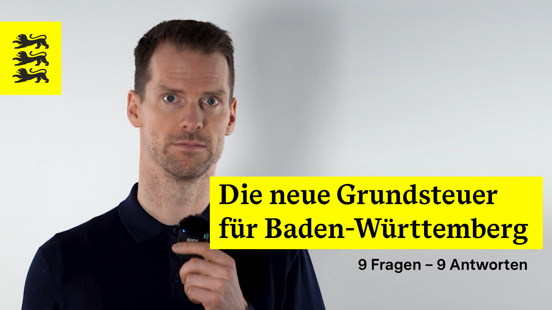 Das Bild zeigt den aktuellen Pressesprecher vom Finanzministerium vor einem neutralen Hintergrund. Er hält ein Mikrofon in der Hand und blickt direkt in die Kamera. Links oben im Bild befindet sich das Wappen von Baden-Württemberg mit den drei schwarzen Löwen auf gelbem Hintergrund. Rechts im Bild steht in großer, gelber Schrift „Die neue Grundsteuer für Baden-Württemberg“ und darunter in kleinerer Schrift „9 Fragen – 9 Antworten“.